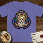 How Great Thou Bark Coton de Tulear T-Shirt flat lay in Violet, featuring a full-color stained-glass saint window of a sable and white Coton de Tulear facing forward, haloed in golden light.