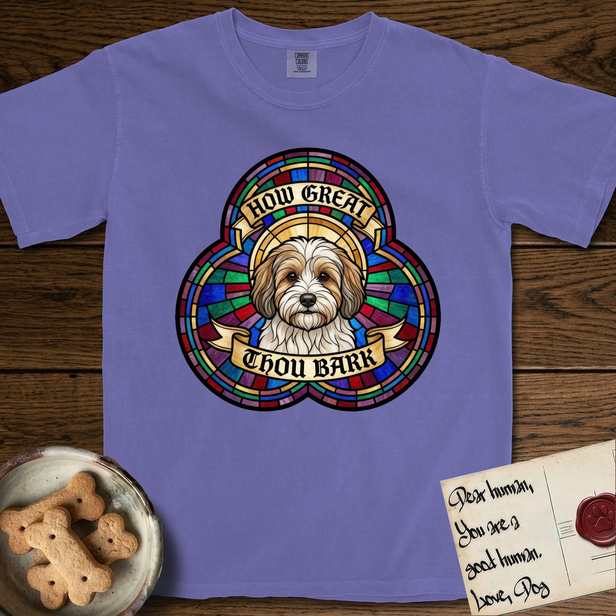 How Great Thou Bark Coton de Tulear T-Shirt flat lay in Violet, featuring a full-color stained-glass saint window of a sable and white Coton de Tulear facing forward, haloed in golden light.