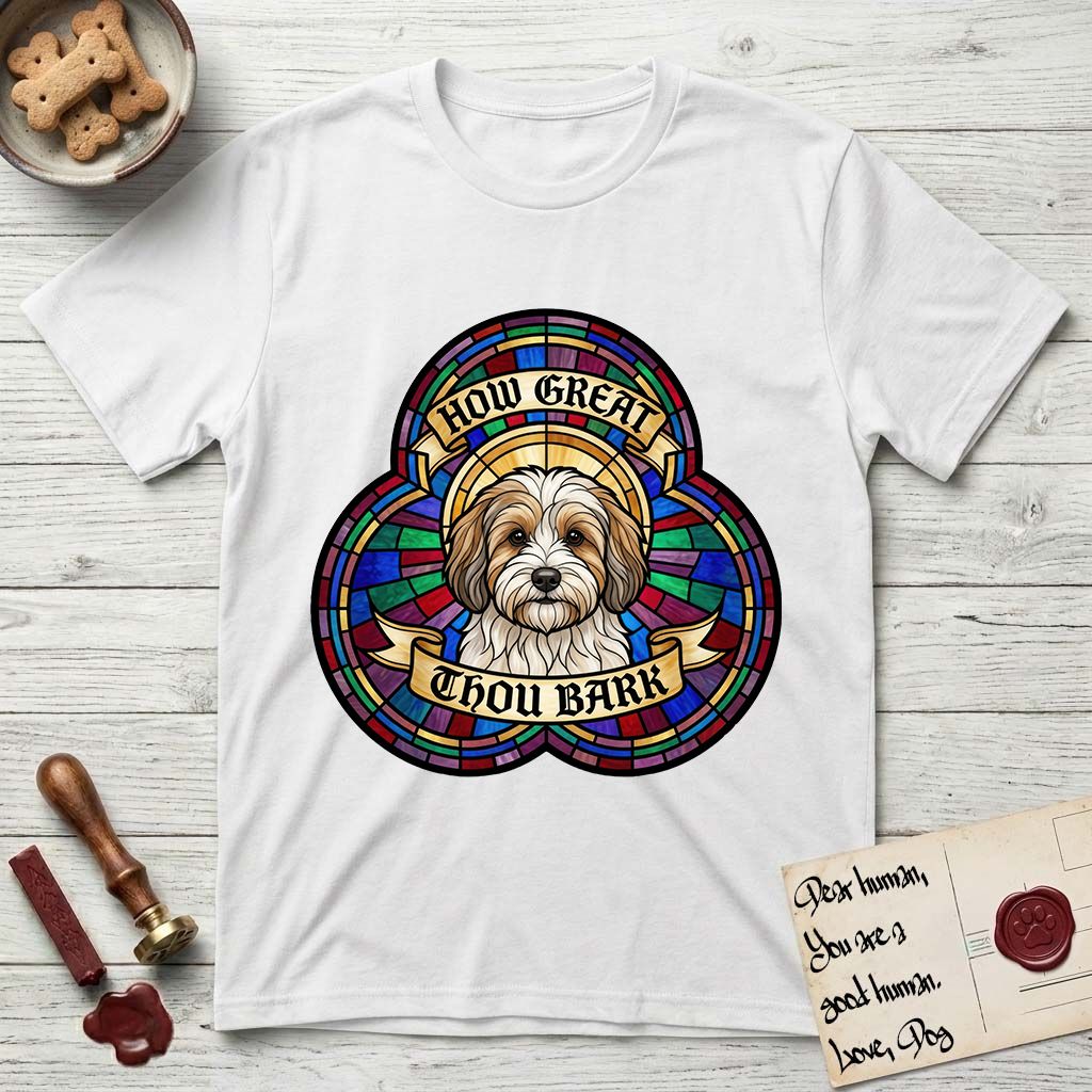 How Great Thou Bark Coton de Tulear T-Shirt flat lay in White, featuring a full-color stained-glass saint window of a sable and white Coton de Tulear facing forward, haloed in golden light.