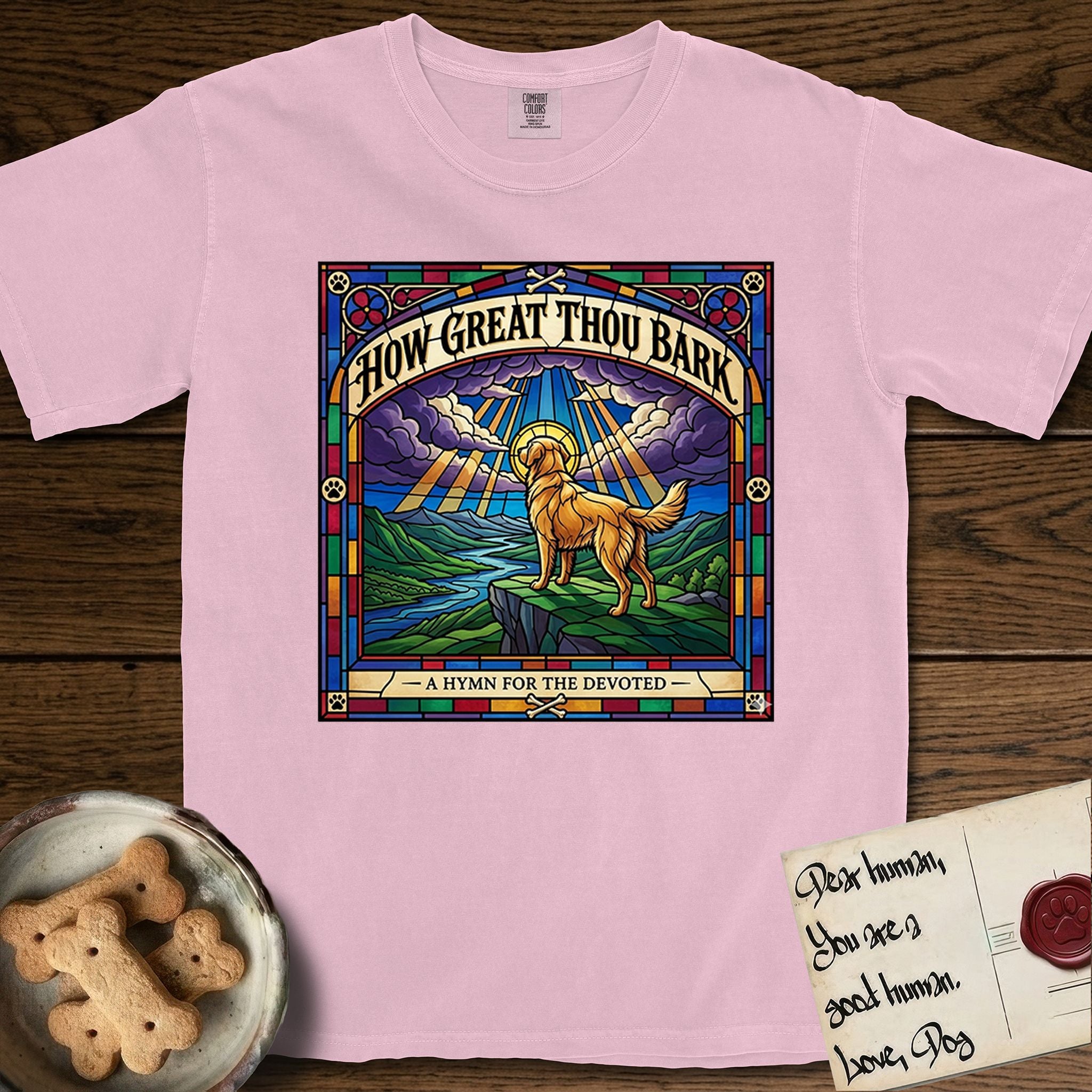 How Great Thou Bark Golden Retriever T-Shirt flat lay in Blossom, featuring a full-color stained-glass saint window of a Golden Retriever standing on a mountain with light breaking through the clouds and a halo.