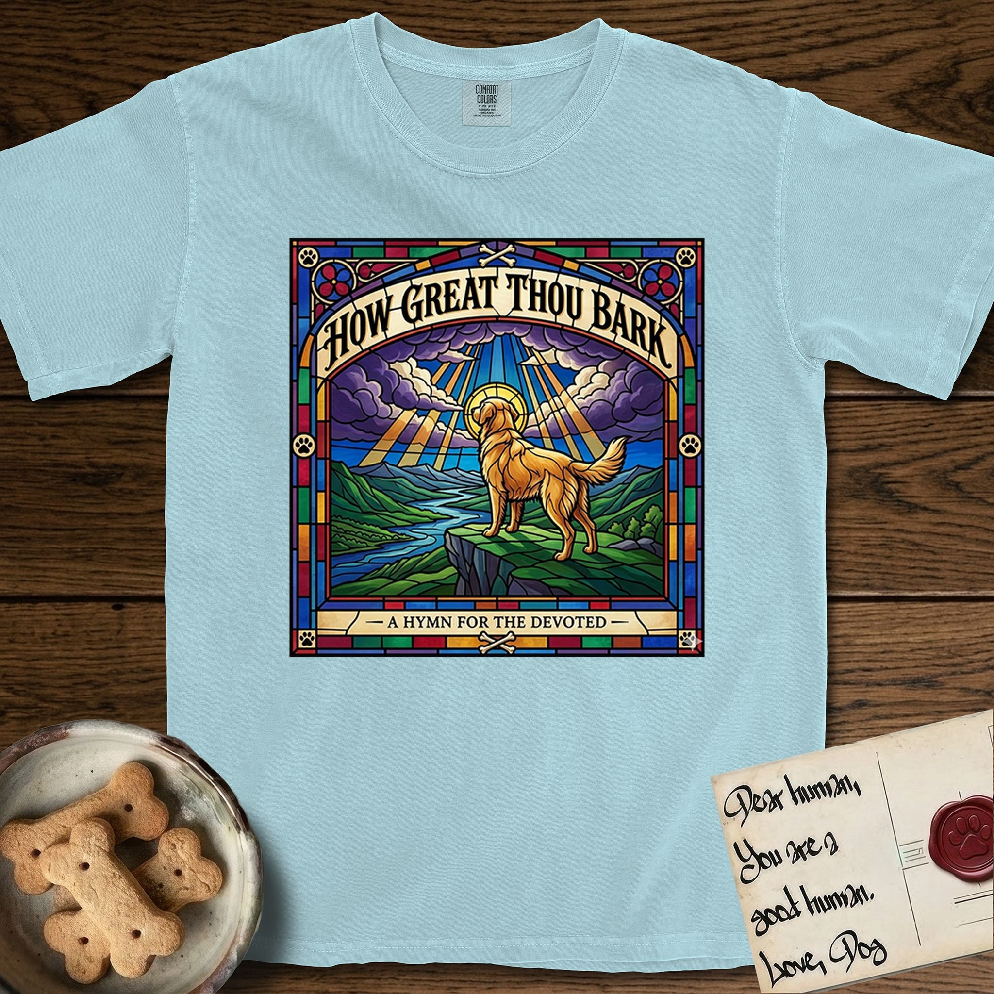 How Great Thou Bark Golden Retriever T-Shirt flat lay in Chambray, featuring a full-color stained-glass saint window of a Golden Retriever standing on a mountain with light breaking through the clouds and a halo.