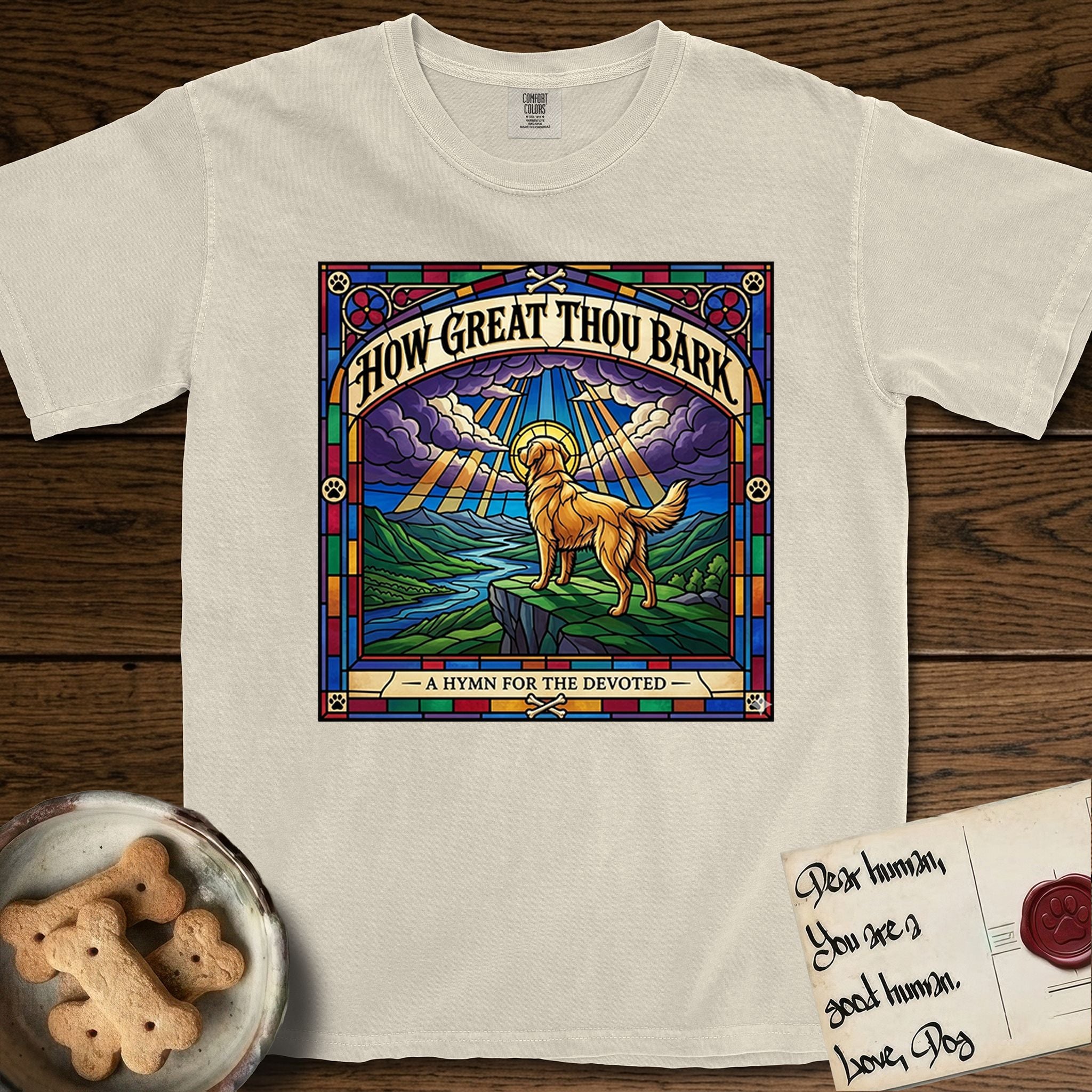 How Great Thou Bark Golden Retriever T-Shirt flat lay in Ivory, featuring a full-color stained-glass saint window of a Golden Retriever standing on a mountain with light breaking through the clouds and a halo.