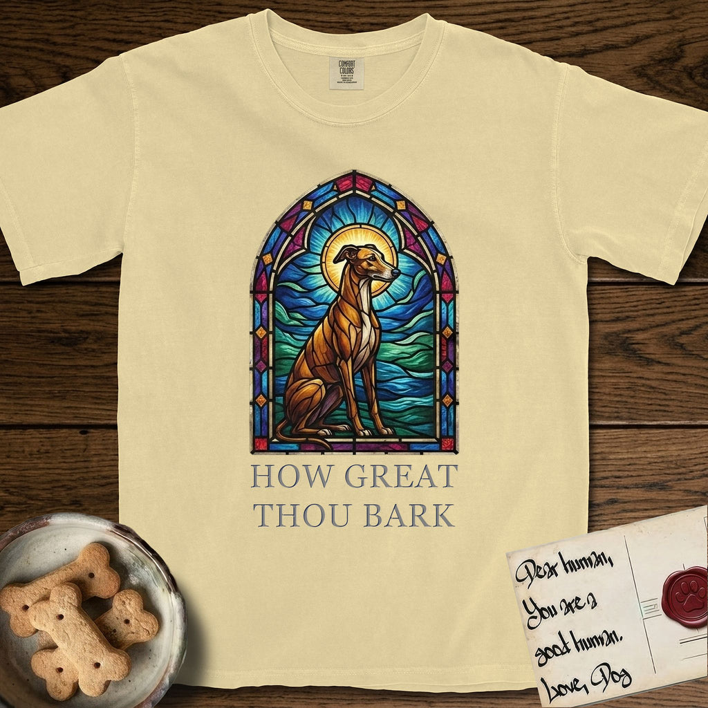 How Great Thou Bark Greyhound T-Shirt flat lay in Butter, featuring a full-color stained-glass saint window of a Greyhound sitting in stillness, with a halo.