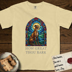 How Great Thou Bark Greyhound T-Shirt flat lay in Butter, featuring a full-color stained-glass saint window of a Greyhound sitting in stillness, with a halo.