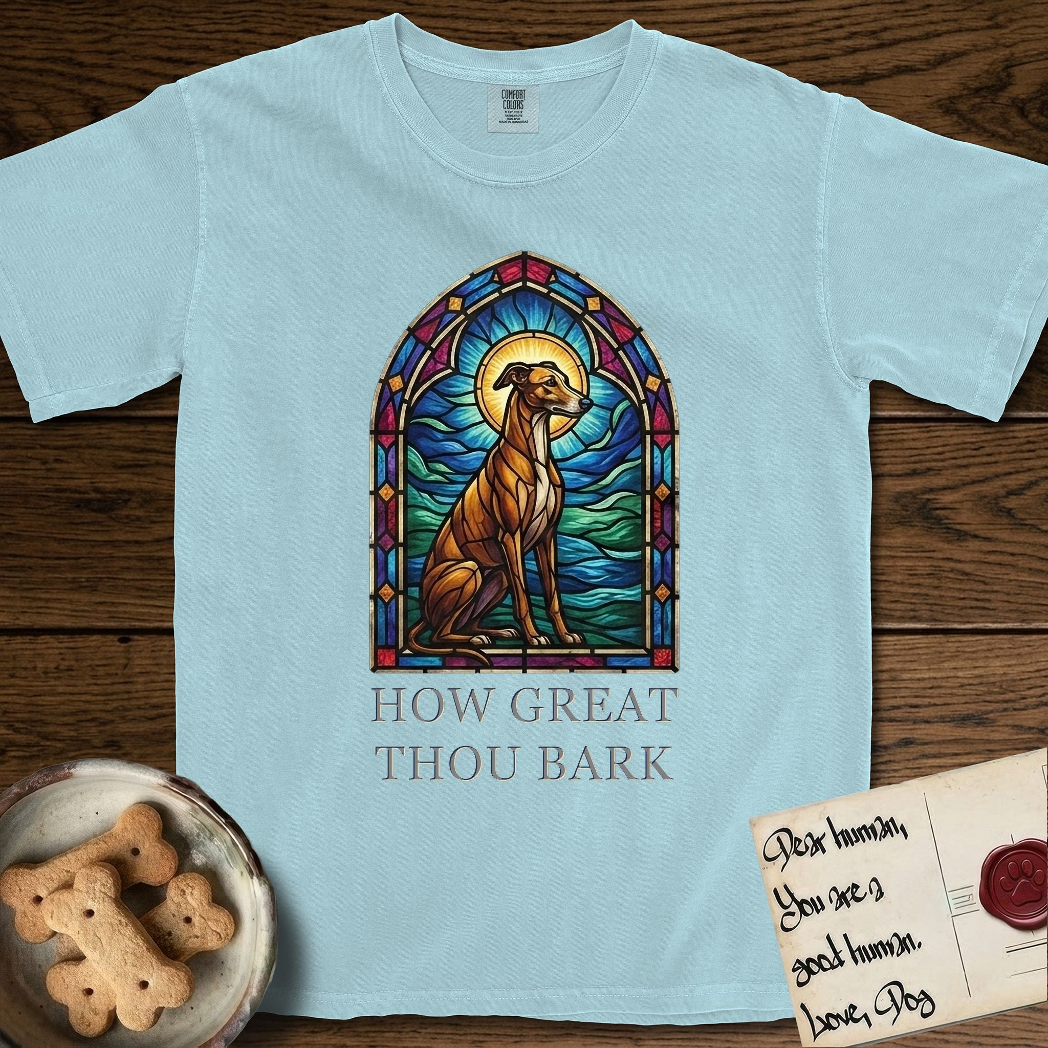 How Great Thou Bark Greyhound T-Shirt flat lay in Chambray, featuring a full-color stained-glass saint window of a Greyhound sitting in stillness, with a halo.
