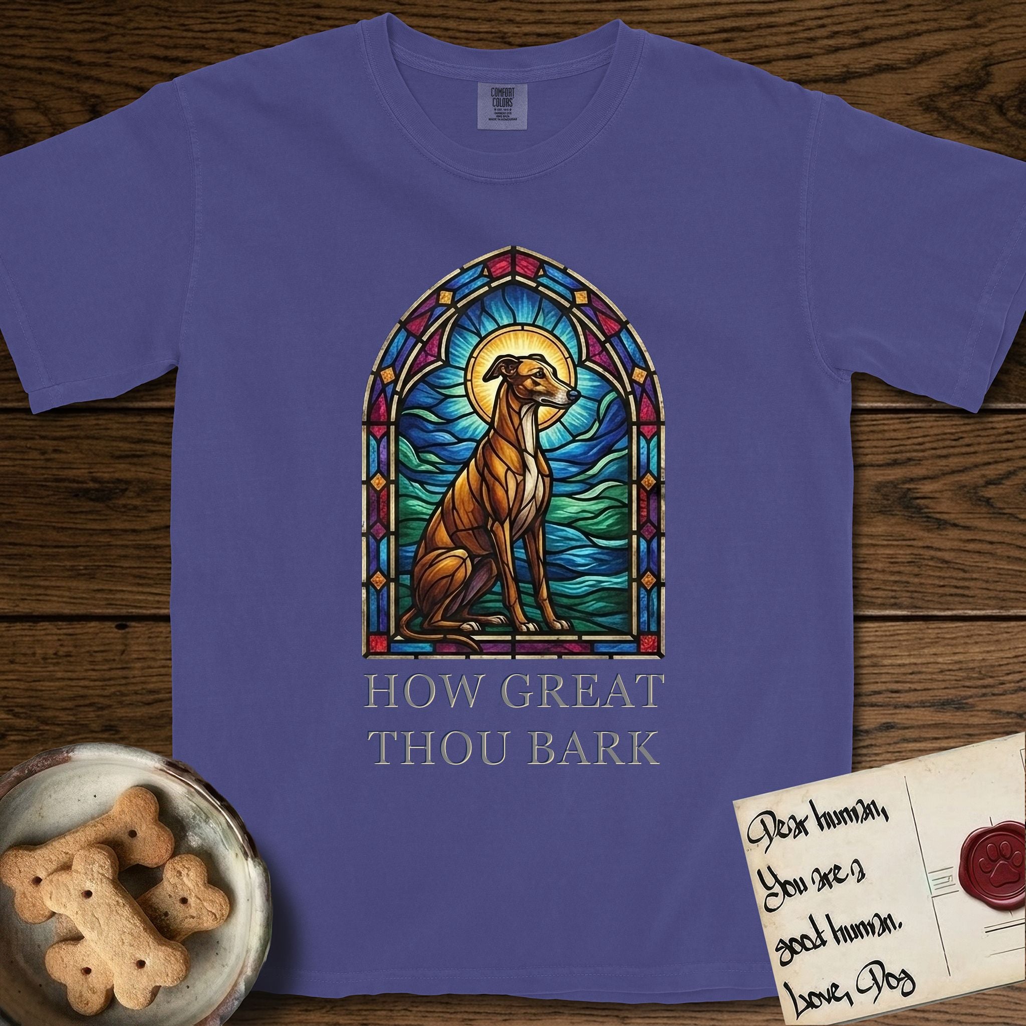 How Great Thou Bark Greyhound T-Shirt flat lay in Grape, featuring a full-color stained-glass saint window of a Greyhound sitting in stillness, with a halo.