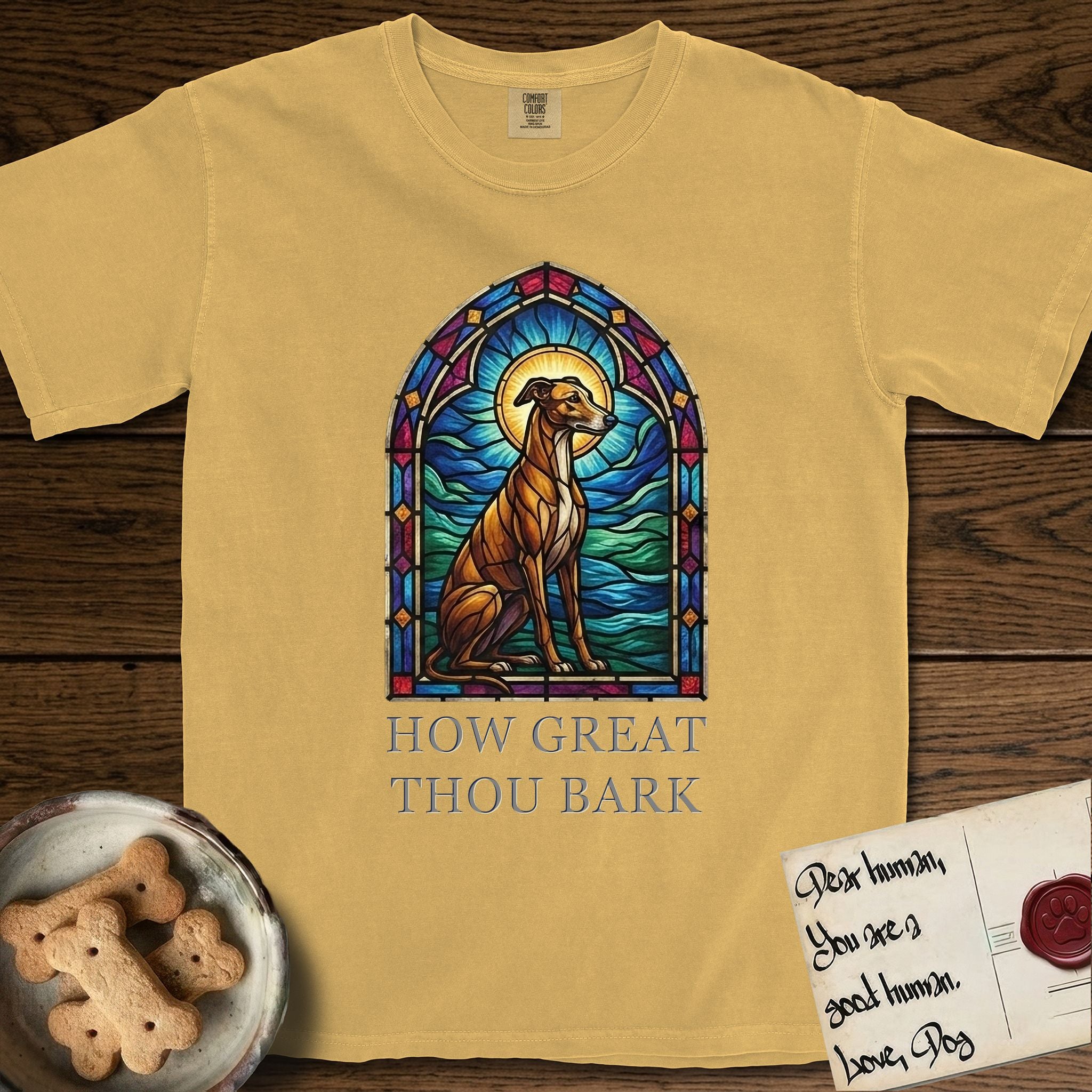 How Great Thou Bark Greyhound T-Shirt flat lay in Mustard, featuring a full-color stained-glass saint window of a Greyhound sitting in stillness, with a halo.