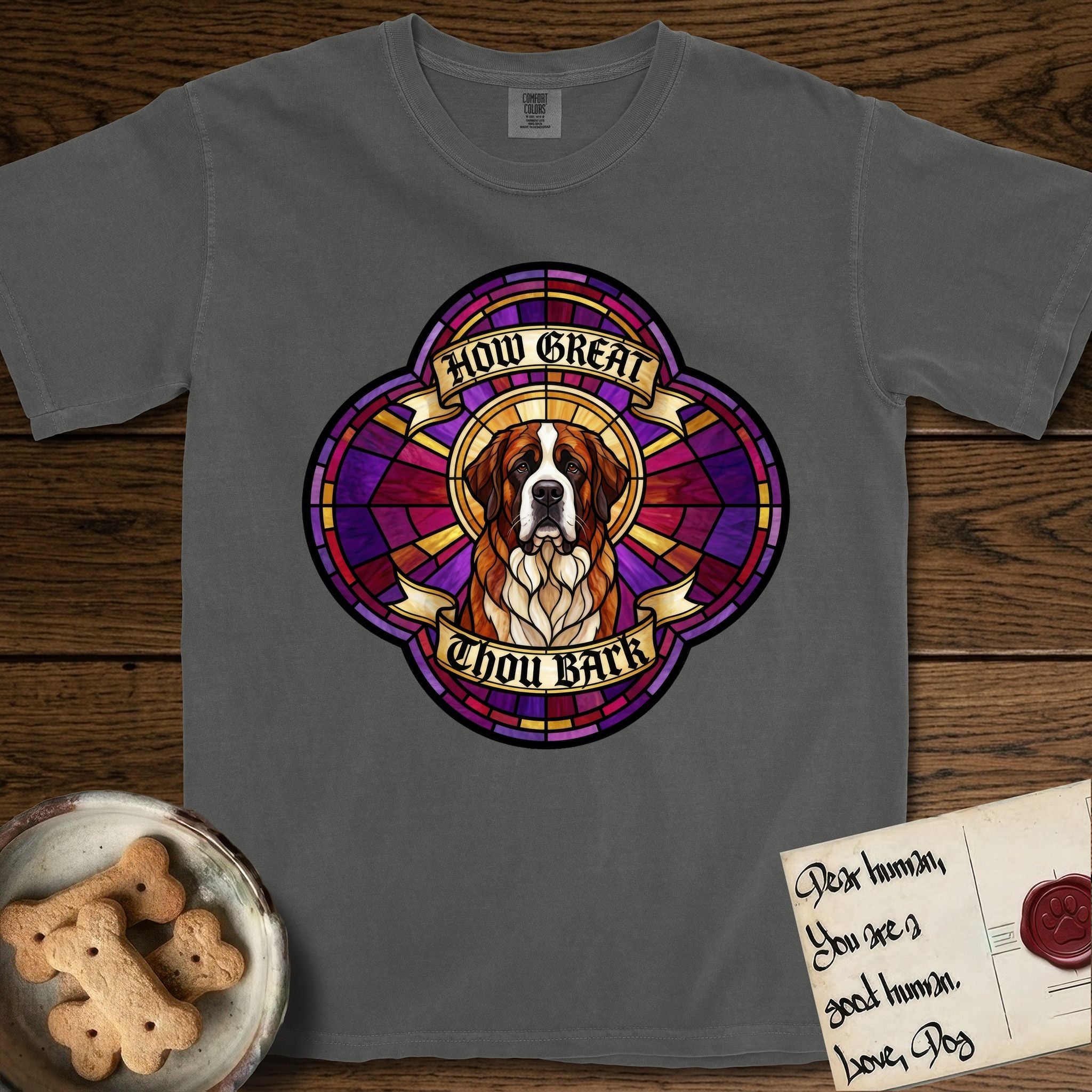How Great Thou Bark Saint Bernard T-Shirt flat lay in Pepper, featuring a full-color stained-glass saint window of a red and white Saint Bernard facing forward, haloed in golden light.