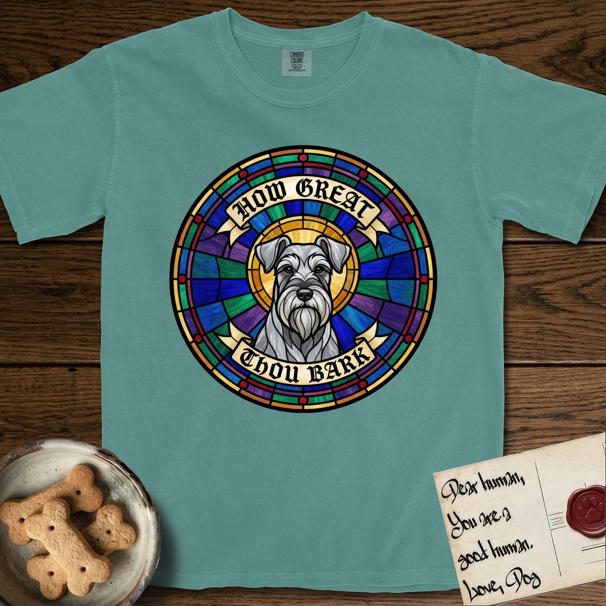 How Great Thou Bark Schnauzer T-Shirt flat lay in Blue Spruce, featuring a full-color stained-glass saint window of a salt-and-pepper Schnauzer with bushy eyebrows and beard, haloed in golden light.
