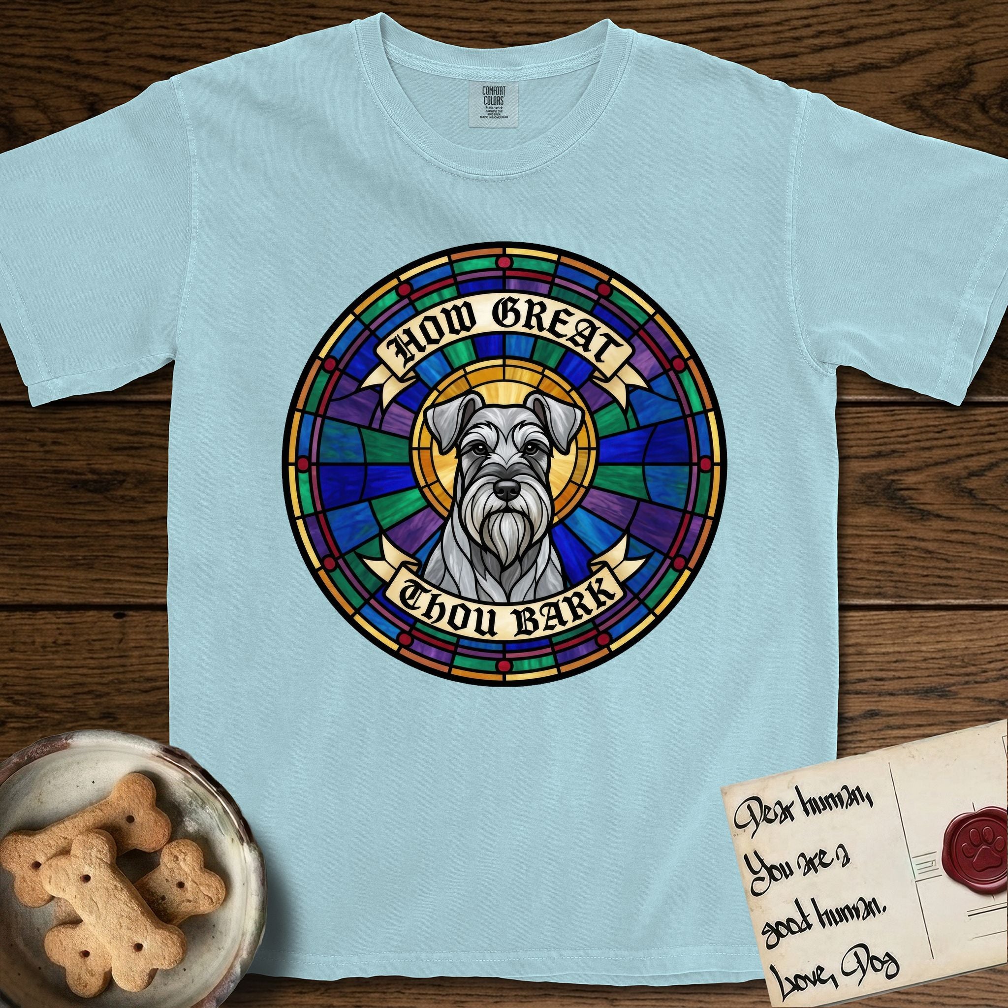 How Great Thou Bark Schnauzer T-Shirt flat lay in Chambray, featuring a full-color stained-glass saint window of a salt-and-pepper Schnauzer with bushy eyebrows and beard, haloed in golden light.