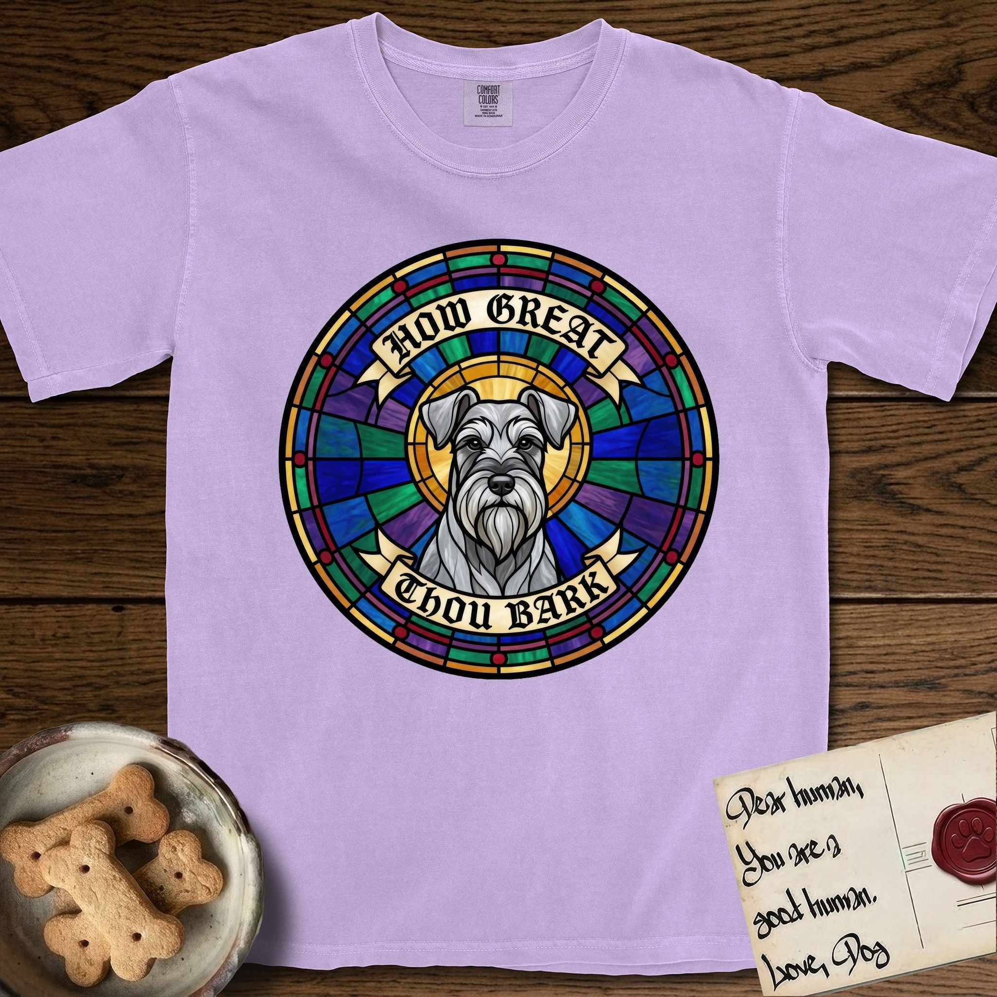 How Great Thou Bark Schnauzer T-Shirt flat lay in Orchid, featuring a full-color stained-glass saint window of a salt-and-pepper Schnauzer with bushy eyebrows and beard, haloed in golden light.