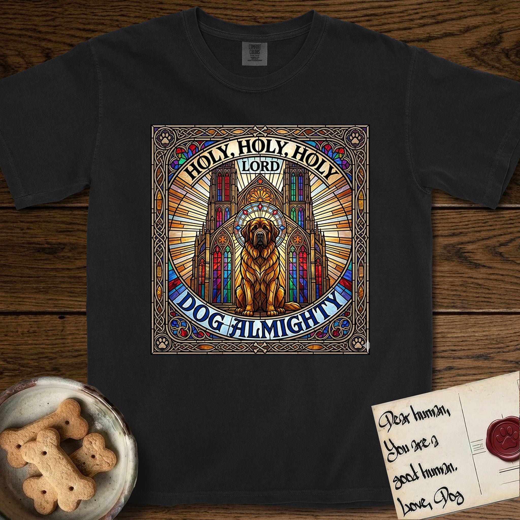 Holy Holy Holy Newfoundland T-Shirt flat lay in Black, featuring a gothic stained-glass window in jewel tones with a Newfoundland at center, Celtic knotwork border, corner paw prints, and the words Holy Holy Holy and Dog Almighty.