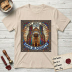 Holy Holy Holy Newfoundland T-Shirt flat lay in Sand, featuring a gothic stained-glass window in jewel tones with a Newfoundland at center, Celtic knotwork border, corner paw prints, and the words Holy Holy Holy and Dog Almighty.