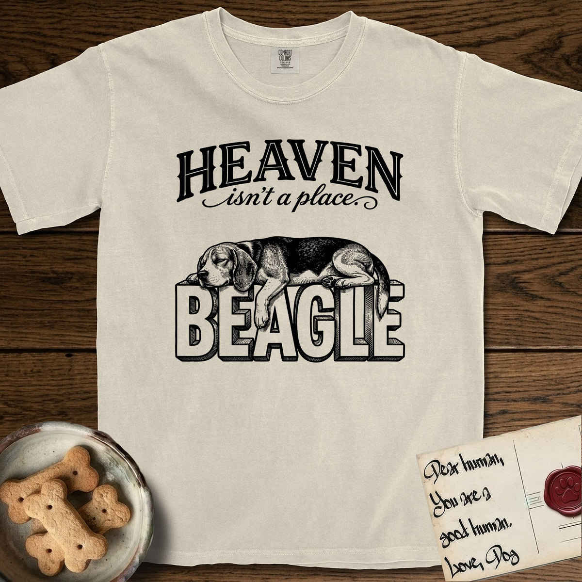 Heaven Isn't a Place Beagle T-Shirt flat lay in Ivory, featuring Black ink engraving illustration of a tricolor Beagle asleep on top of the giant carved block letters BEAGLE, under the lettering HEAVEN isn't a place..