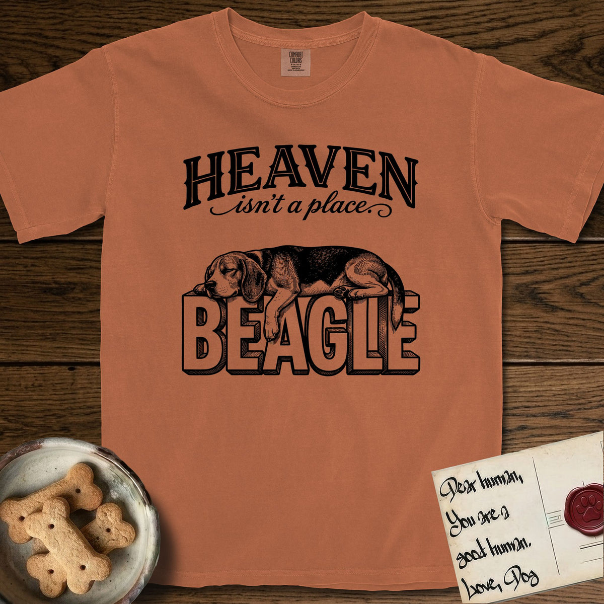 Heaven Isn't a Place Beagle T-Shirt flat lay in Yam, featuring Black ink engraving illustration of a tricolor Beagle asleep on top of the giant carved block letters BEAGLE, under the lettering HEAVEN isn't a place..