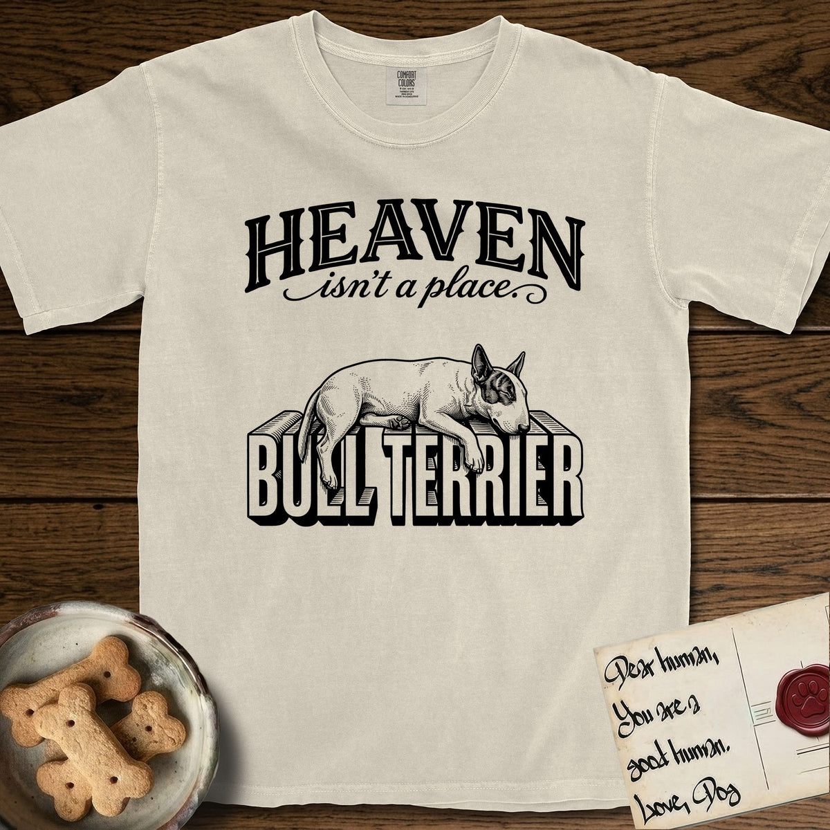 Heaven Isn't a Place Bull Terrier T-Shirt flat lay in Ivory, featuring Black ink engraving illustration of a Bull Terrier with a dark patch over one eye asleep on top of the giant carved block letters BULL TERRIER, under the lettering HEAVEN isn't a place..