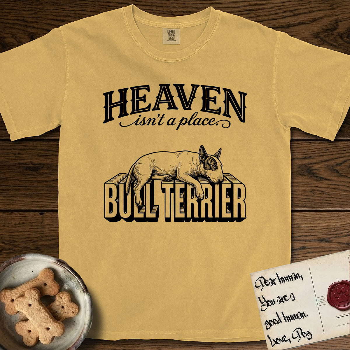 Heaven Isn't a Place Bull Terrier T-Shirt flat lay in Mustard, featuring Black ink engraving illustration of a Bull Terrier with a dark patch over one eye asleep on top of the giant carved block letters BULL TERRIER, under the lettering HEAVEN isn't a place..