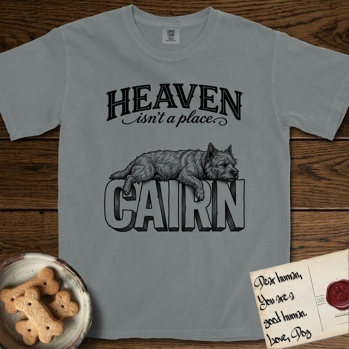 Heaven Isn't a Place Cairn Terrier T-Shirt flat lay in Granite, featuring Black ink engraving illustration of a shaggy Cairn Terrier asleep on top of the giant carved block letters CAIRN, under the lettering HEAVEN isn't a place..