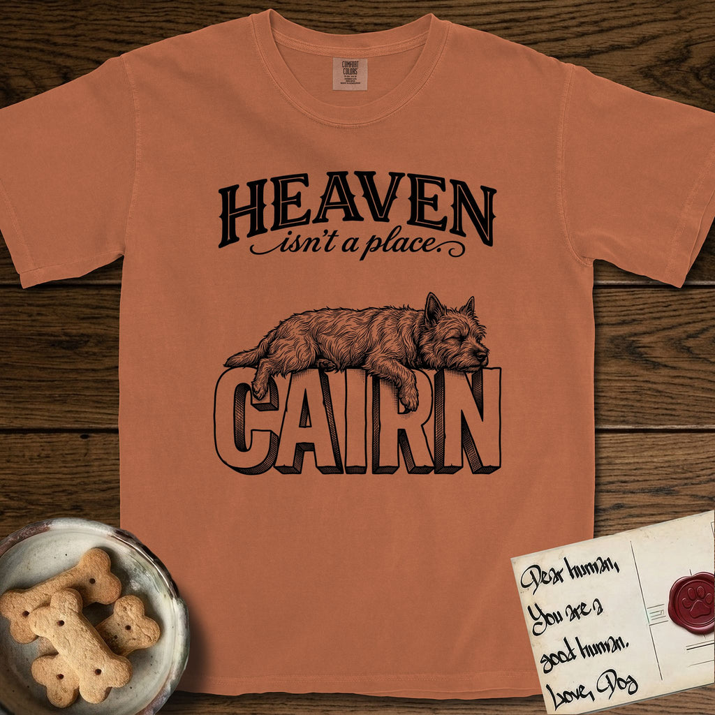Heaven Isn't a Place Cairn Terrier T-Shirt flat lay in Yam, featuring Black ink engraving illustration of a shaggy Cairn Terrier asleep on top of the giant carved block letters CAIRN, under the lettering HEAVEN isn't a place..