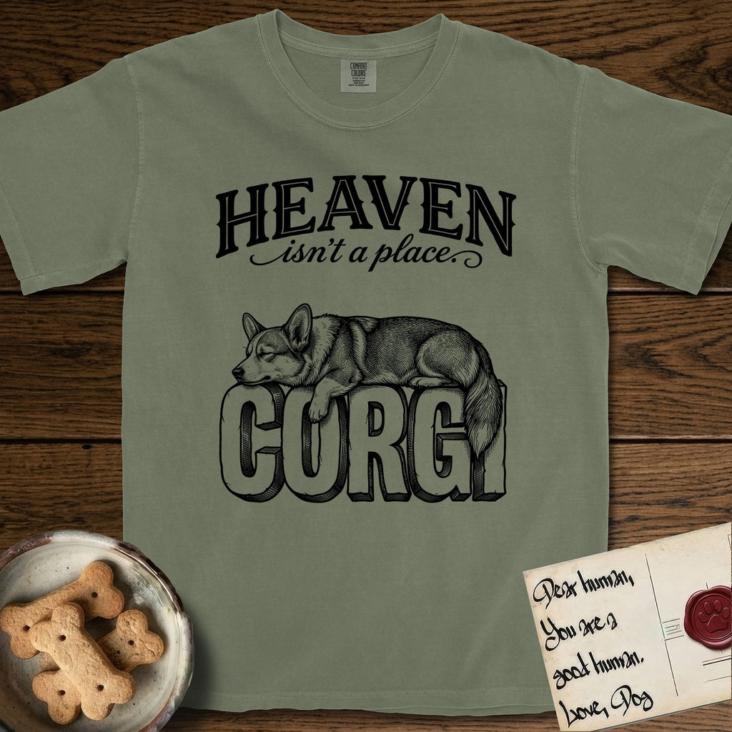 Heaven Isn't a Place Corgi T-Shirt flat lay in Sage, featuring Black ink engraving illustration of a Corgi with a long fluffy tail asleep on top of the giant carved block letters CORGI, under the lettering HEAVEN isn't a place..