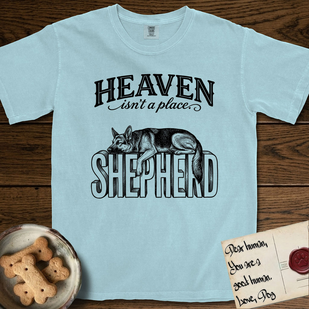 Heaven Isn't a Place German Shepherd T-Shirt flat lay in Chambray, featuring Black ink engraving illustration of a German Shepherd asleep on top of the giant carved block letters SHEPHERD, under the lettering HEAVEN isn't a place..