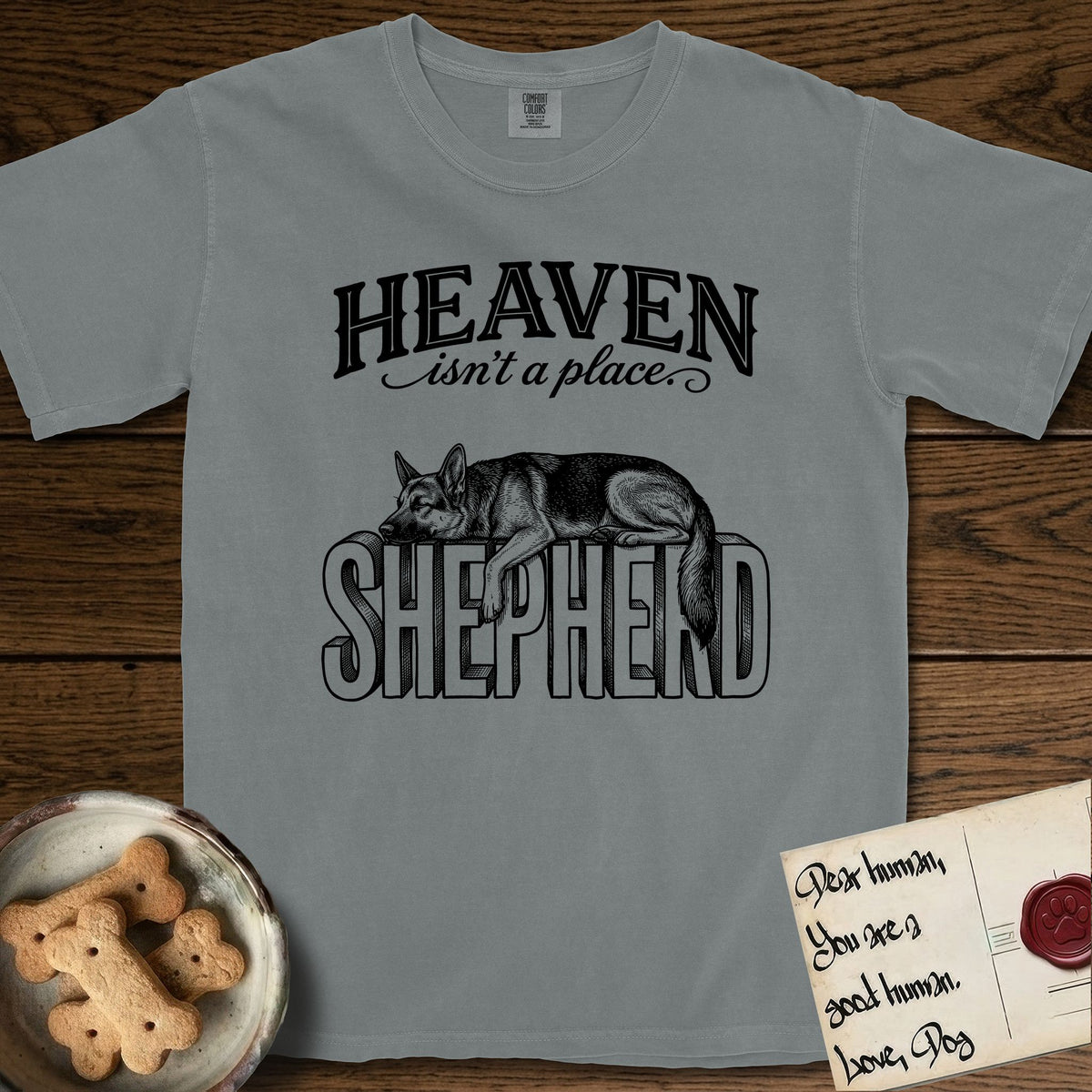 Heaven Isn't a Place German Shepherd T-Shirt flat lay in Granite, featuring Black ink engraving illustration of a German Shepherd asleep on top of the giant carved block letters SHEPHERD, under the lettering HEAVEN isn't a place..