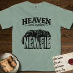 Heaven Isn't a Place Newfoundland T-Shirt flat lay in Bay, featuring Black ink engraving illustration of a Newfoundland asleep on top of the giant carved block letters NEWFIE, under the lettering HEAVEN isn't a place..