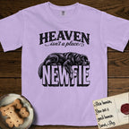 Heaven Isn't a Place Newfoundland T-Shirt flat lay in Orchid, featuring Black ink engraving illustration of a Newfoundland asleep on top of the giant carved block letters NEWFIE, under the lettering HEAVEN isn't a place..