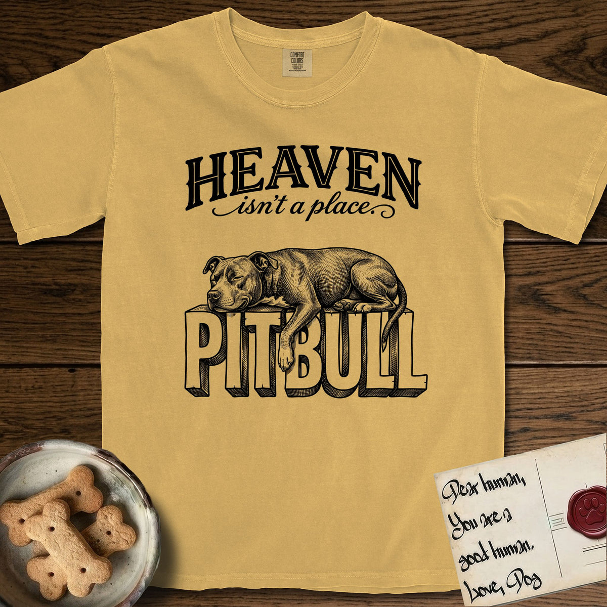 Heaven Isn't a Place Pitbull T-Shirt flat lay in Mustard, featuring Black ink engraving illustration of a Pitbull asleep on top of the giant carved block letters PITBULL, under the lettering HEAVEN isn't a place..