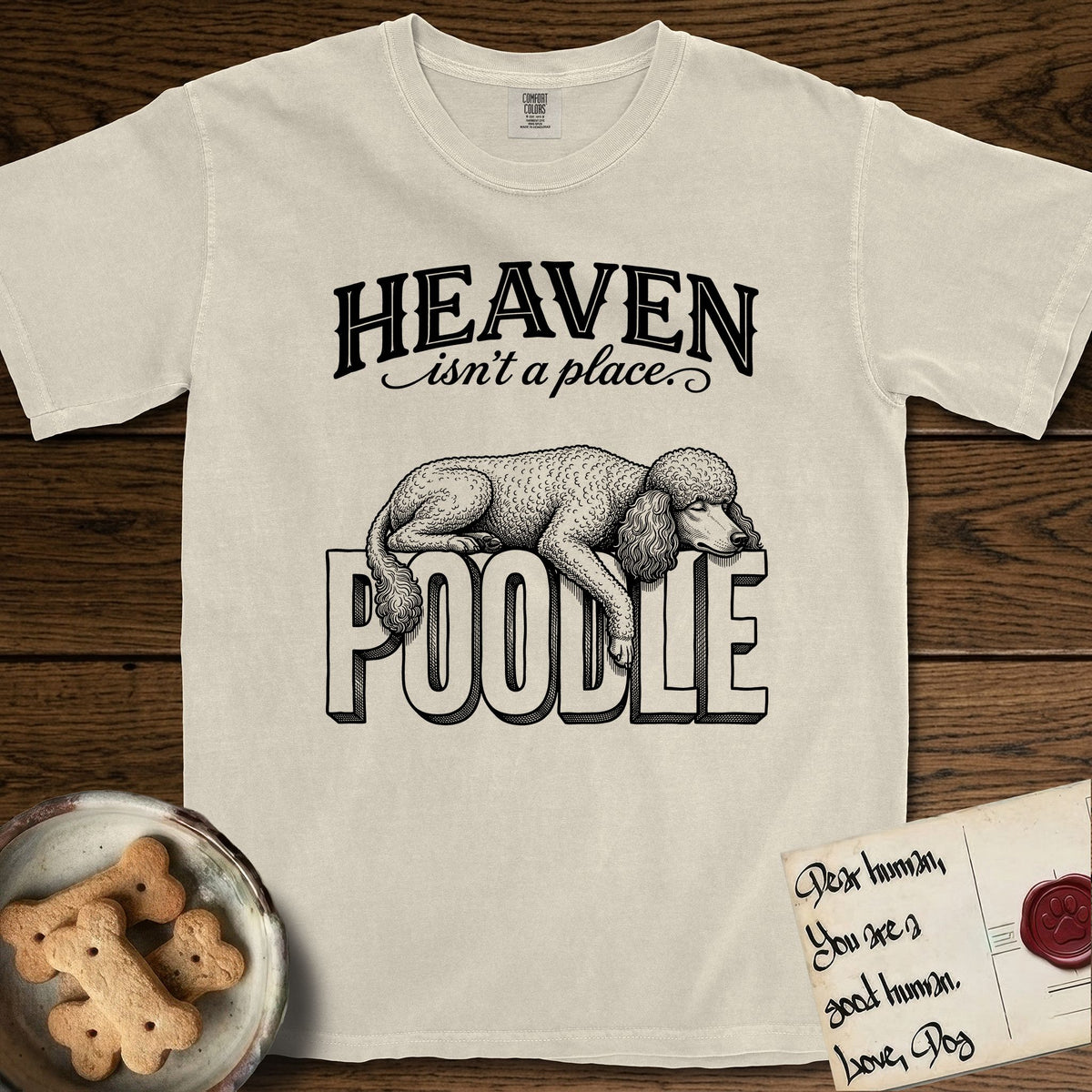 Heaven Isn't a Place Poodle T-Shirt flat lay in Ivory, featuring Black ink engraving illustration of a curly Standard Poodle asleep on top of the giant carved block letters POODLE, under the lettering HEAVEN isn't a place..