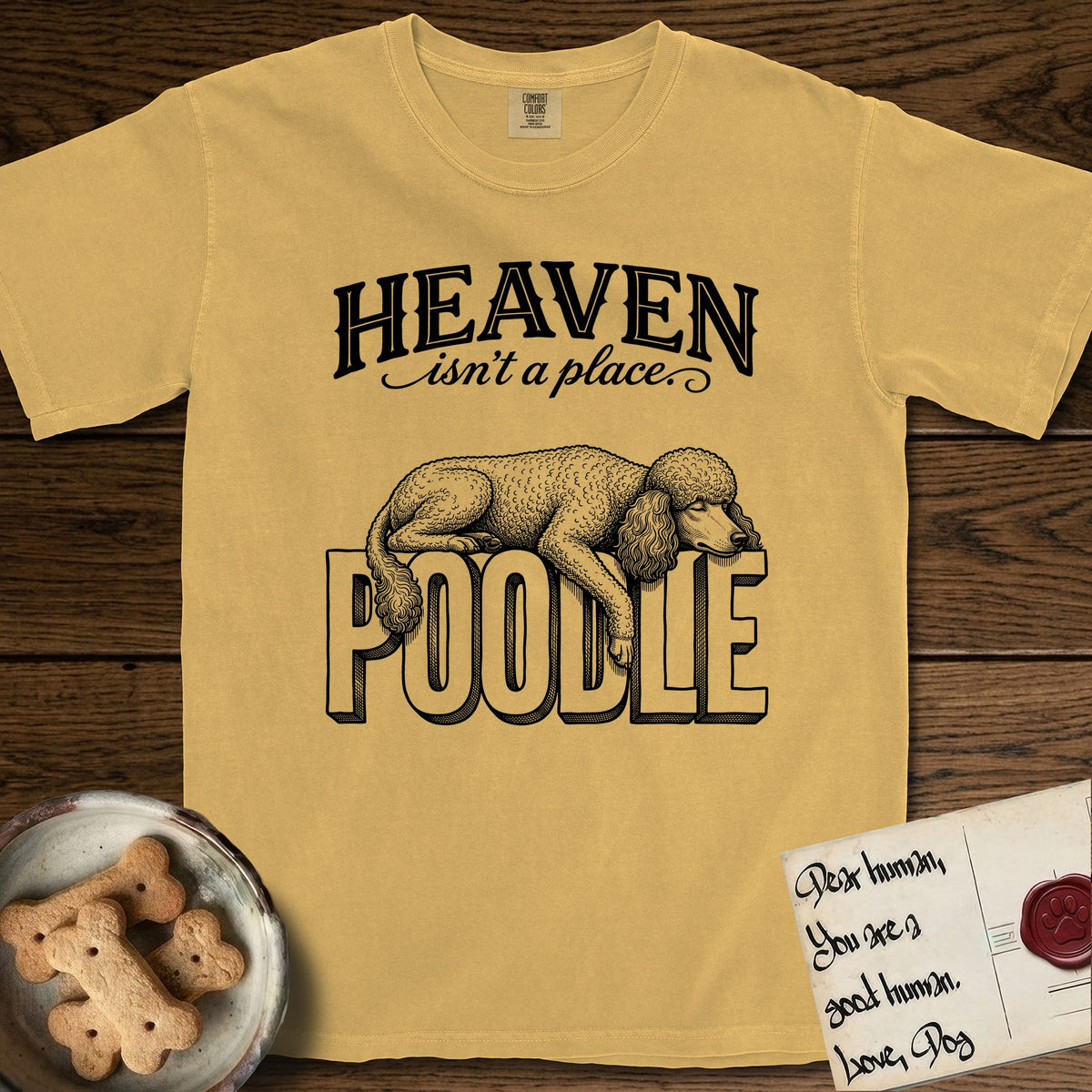 Heaven Isn't a Place Poodle T-Shirt flat lay in Mustard, featuring Black ink engraving illustration of a curly Standard Poodle asleep on top of the giant carved block letters POODLE, under the lettering HEAVEN isn't a place..