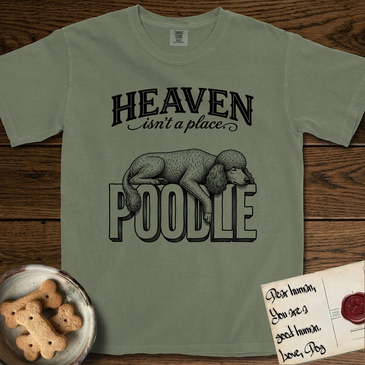 Heaven Isn't a Place Poodle T-Shirt flat lay in Sage, featuring Black ink engraving illustration of a curly Standard Poodle asleep on top of the giant carved block letters POODLE, under the lettering HEAVEN isn't a place..