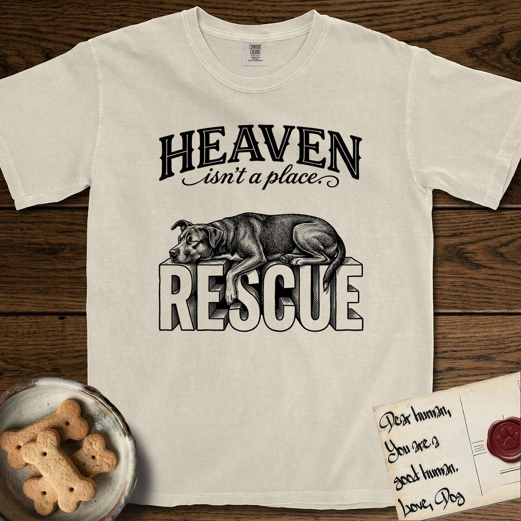 Heaven Isn't a Place Rescue Mutt T-Shirt flat lay in Ivory, featuring Black ink engraving illustration of a rescue Dog that is a Lab, Shepherd and Pitbull mix asleep on top of the giant carved block letters RESCUE, under the lettering HEAVEN isn't a place..