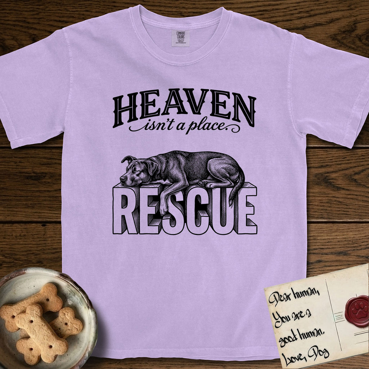 Heaven Isn't a Place Rescue Mutt T-Shirt flat lay in Orchid, featuring Black ink engraving illustration of a rescue Dog that is a Lab, Shepherd and Pitbull mix asleep on top of the giant carved block letters RESCUE, under the lettering HEAVEN isn't a place..