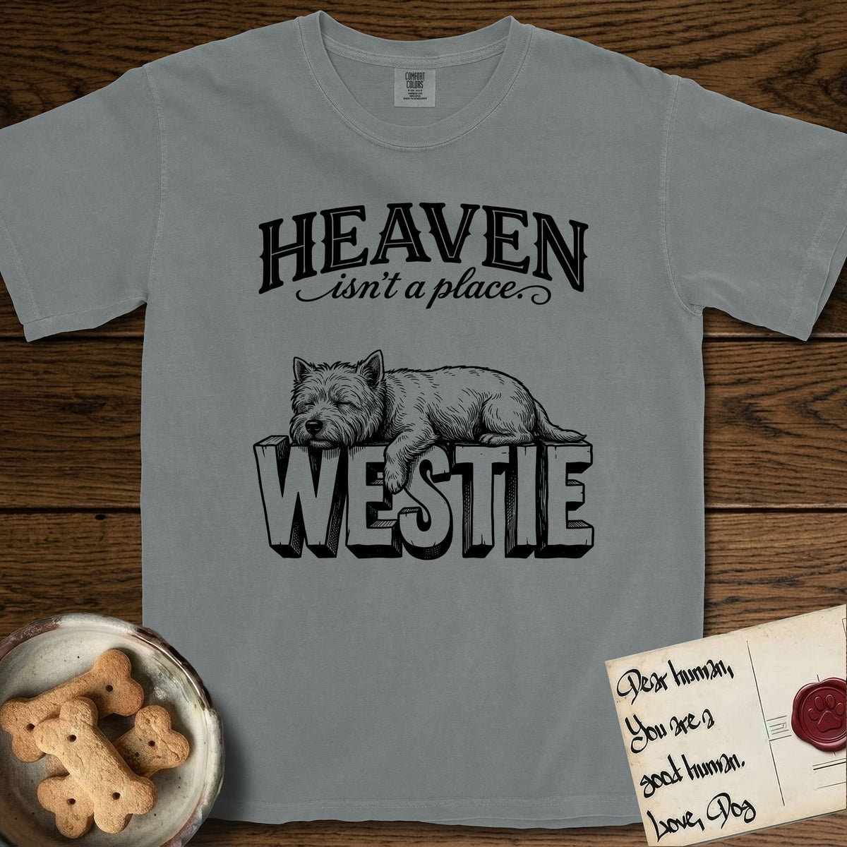 Heaven Isn't a Place Westie T-Shirt flat lay in Granite, featuring Black ink engraving illustration of a Westie asleep on top of the giant carved block letters WESTIE, under the lettering HEAVEN isn't a place..