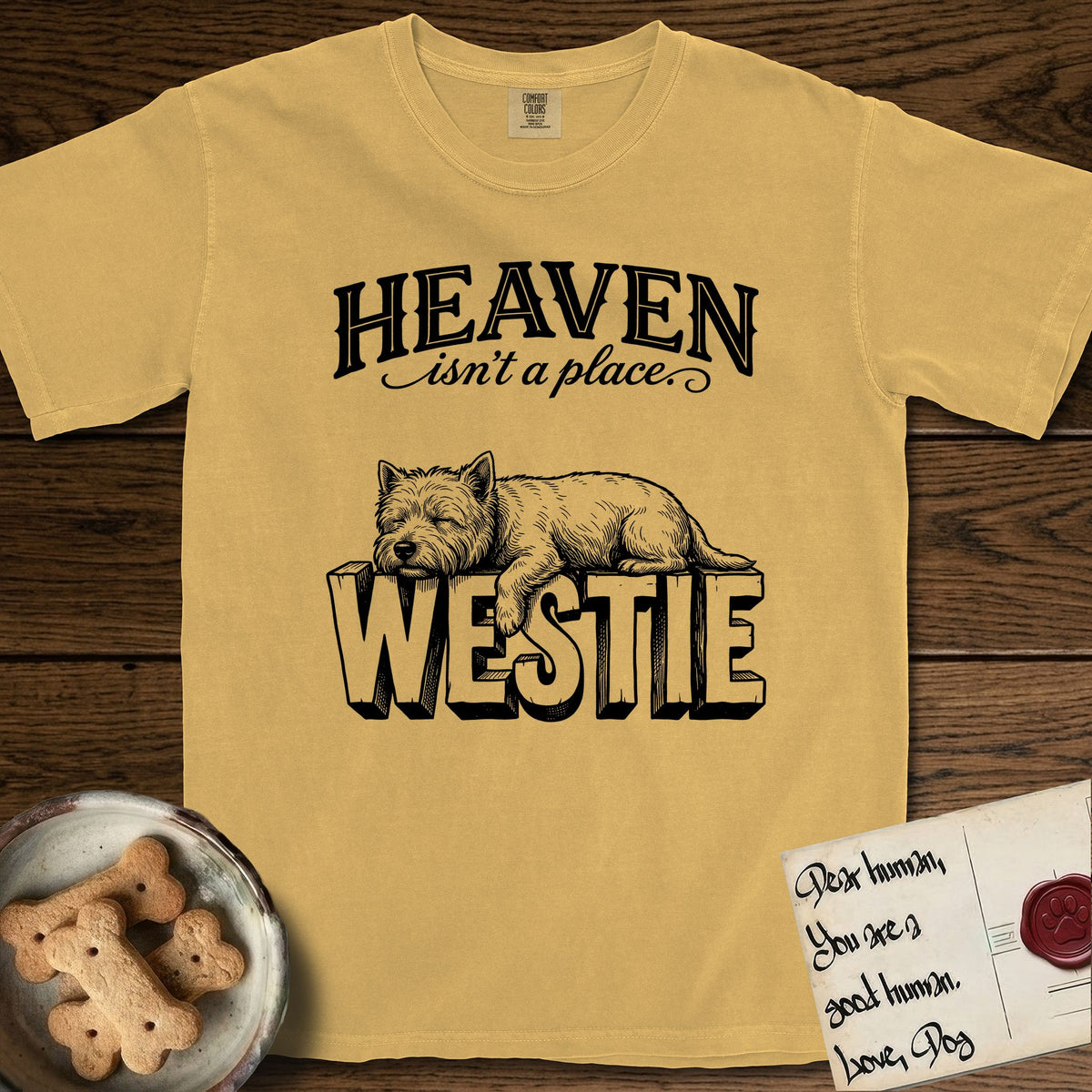 Heaven Isn't a Place Westie T-Shirt flat lay in Mustard, featuring Black ink engraving illustration of a Westie asleep on top of the giant carved block letters WESTIE, under the lettering HEAVEN isn't a place..