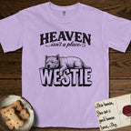 Heaven Isn't a Place Westie T-Shirt flat lay in Orchid, featuring Black ink engraving illustration of a Westie asleep on top of the giant carved block letters WESTIE, under the lettering HEAVEN isn't a place..