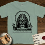Holy Orders Basset Hound T-Shirt flat lay in Bay, featuring a bold black-and-white linocut saint-medallion portrait of a Basset Hound.