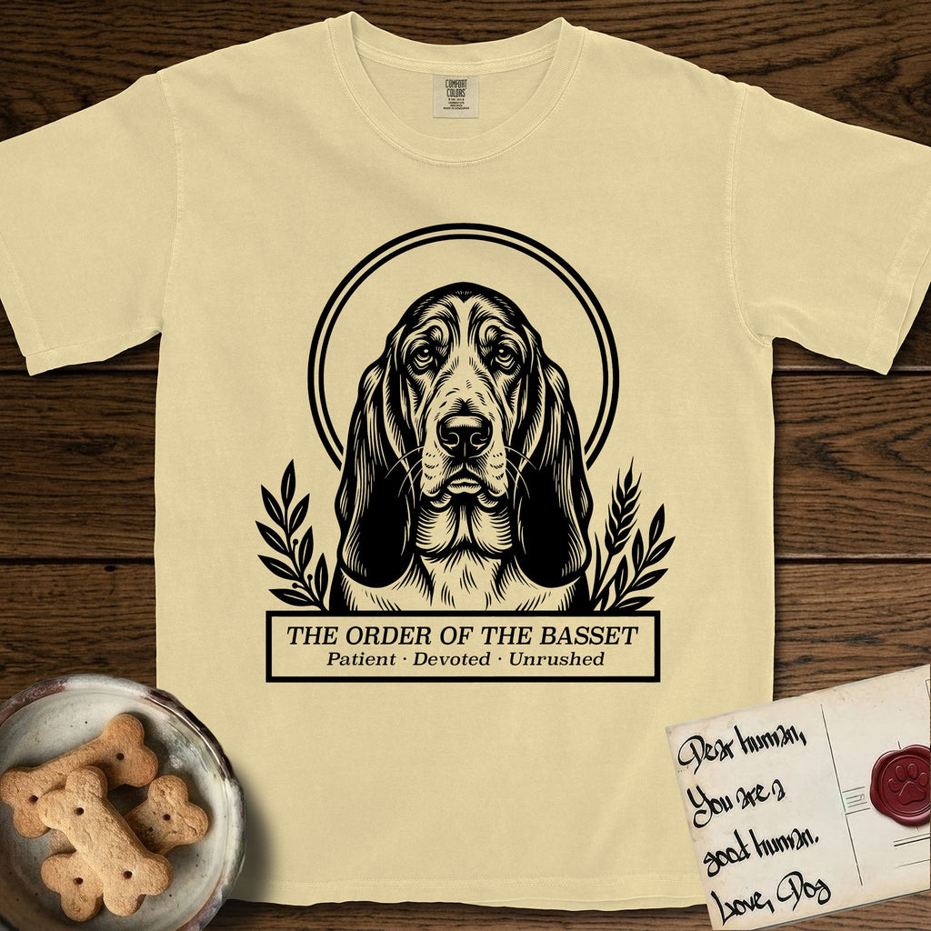 Holy Orders Basset Hound T-Shirt flat lay in Butter, featuring a bold black-and-white linocut saint-medallion portrait of a Basset Hound.