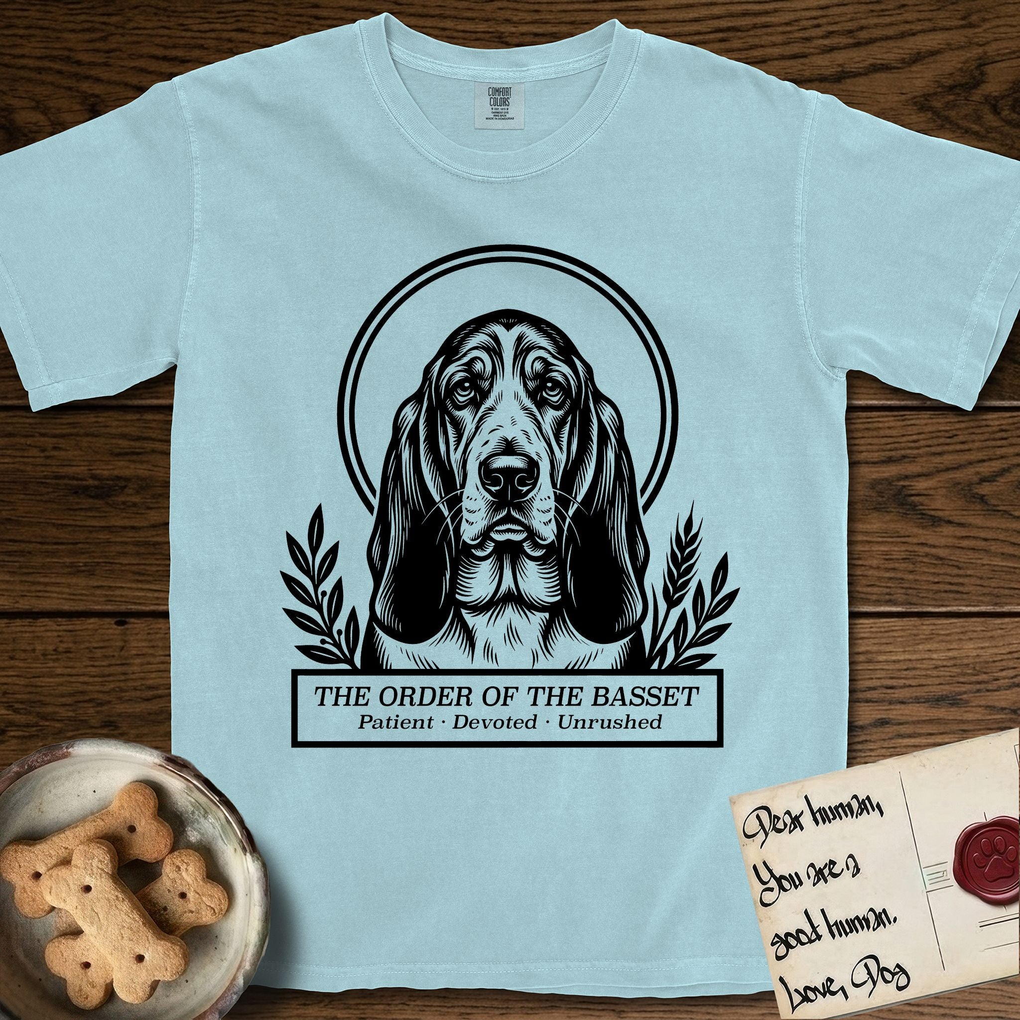 Holy Orders Basset Hound T-Shirt flat lay in Chambray, featuring a bold black-and-white linocut saint-medallion portrait of a Basset Hound.