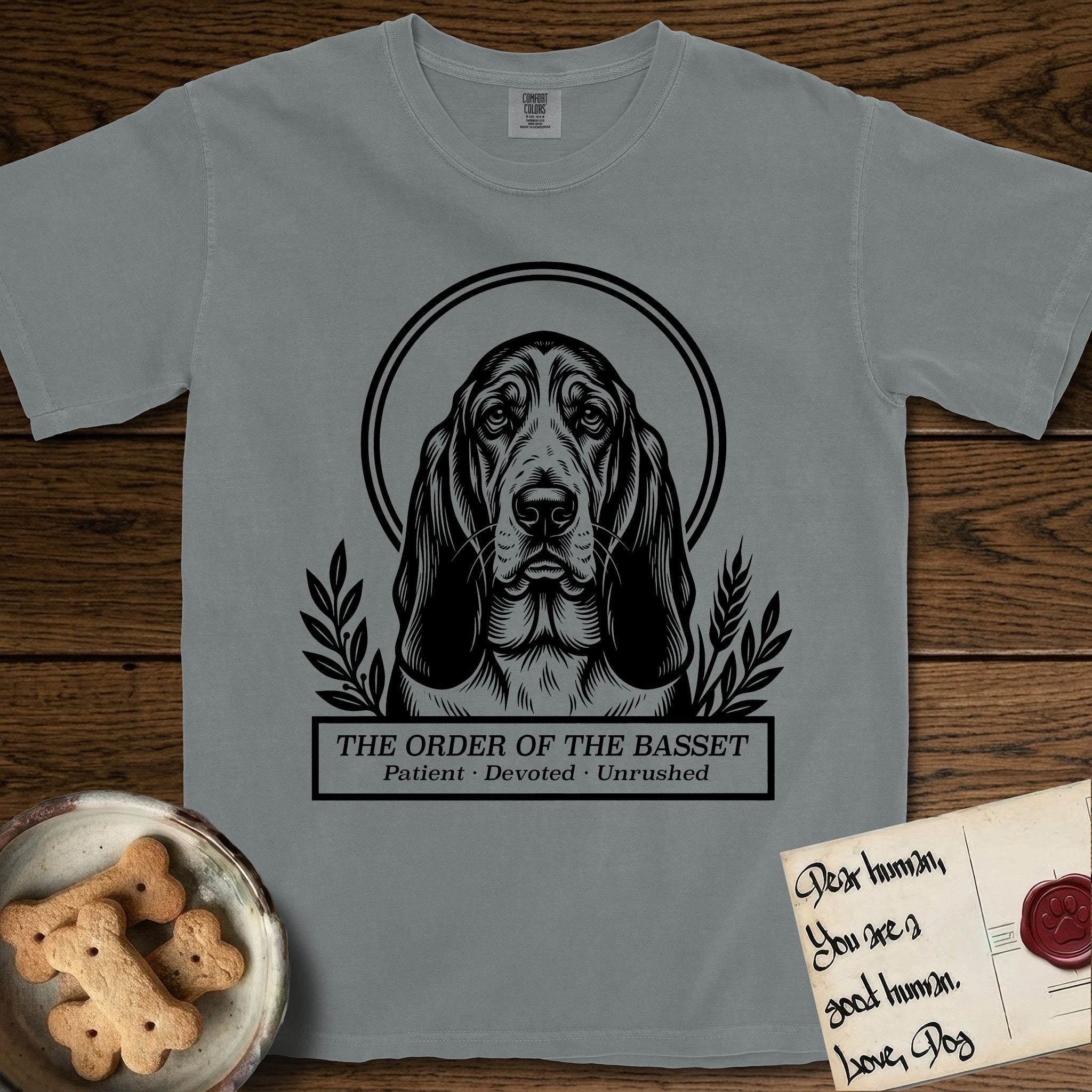 Holy Orders Basset Hound T-Shirt flat lay in Granite, featuring a bold black-and-white linocut saint-medallion portrait of a Basset Hound.