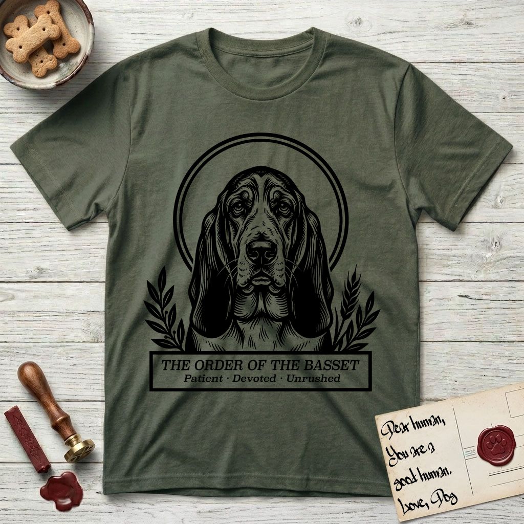 Holy Orders Basset Hound T-Shirt flat lay in Heather Military Green, featuring a bold black-and-white linocut saint-medallion portrait of a Basset Hound.