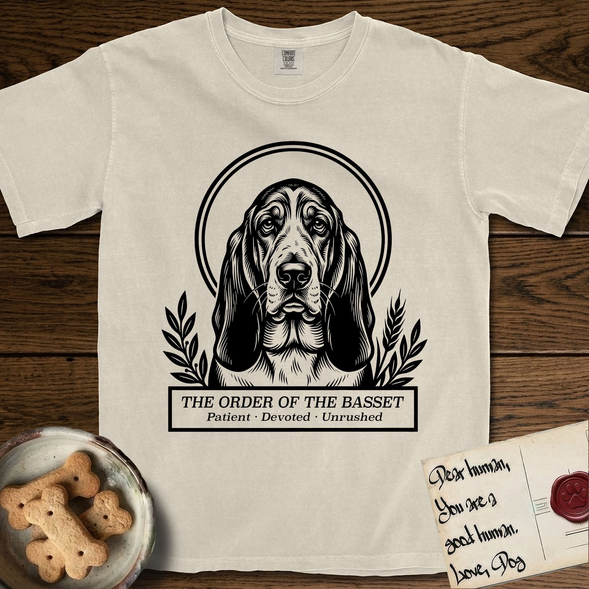 Holy Orders Basset Hound T-Shirt flat lay in Ivory, featuring a bold black-and-white linocut saint-medallion portrait of a Basset Hound.