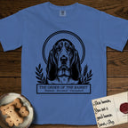 Holy Orders Basset Hound T-Shirt flat lay in Mystic Blue, featuring a bold black-and-white linocut saint-medallion portrait of a Basset Hound.