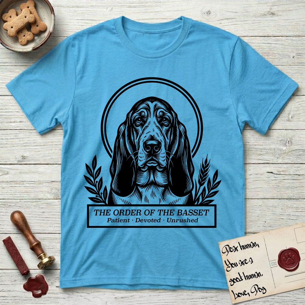 Holy Orders Basset Hound T-Shirt flat lay in Sky, featuring a bold black-and-white linocut saint-medallion portrait of a Basset Hound.