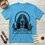 Holy Orders Basset Hound T-Shirt flat lay in Sky, featuring a bold black-and-white linocut saint-medallion portrait of a Basset Hound.