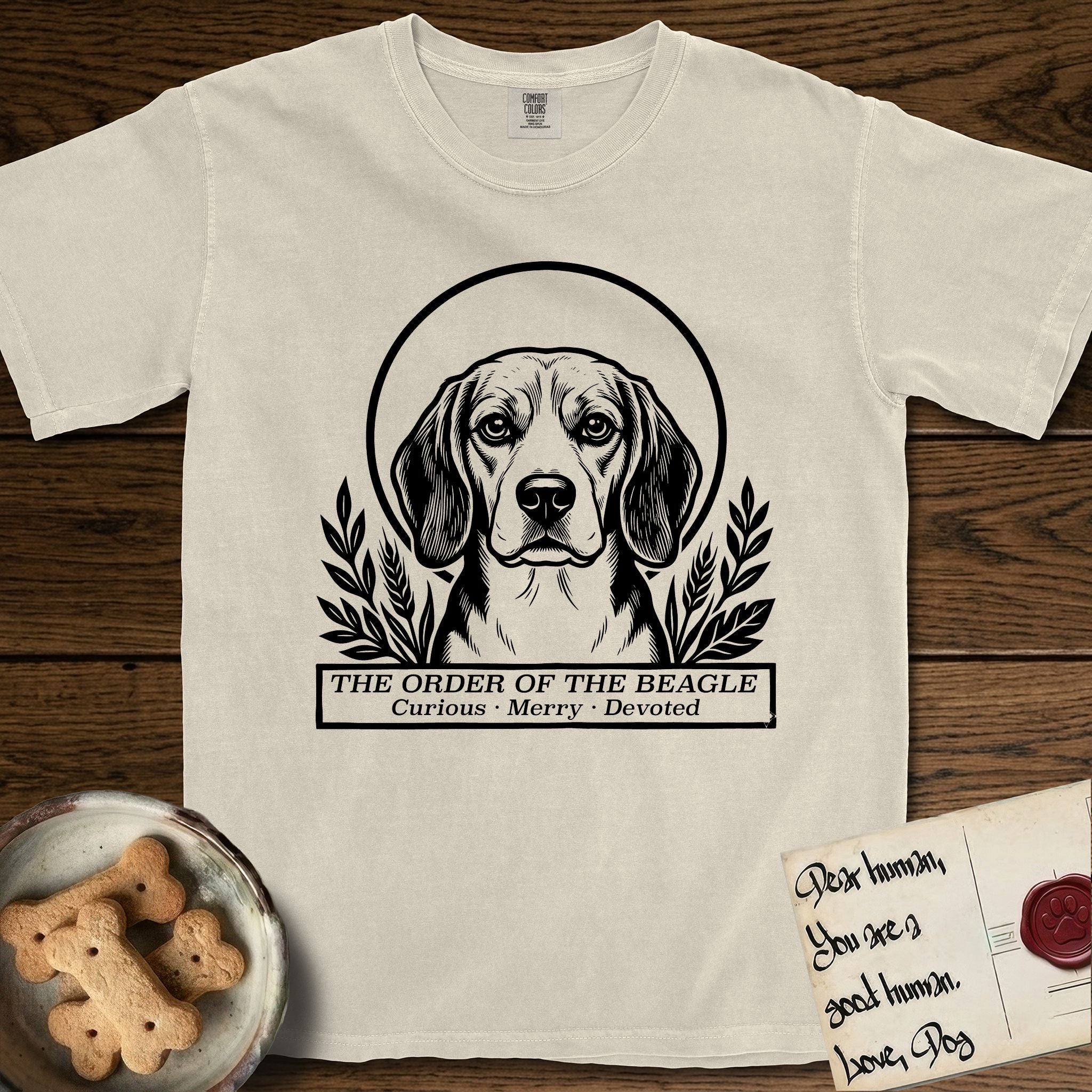 Holy Orders Beagle T-Shirt flat lay in Ivory, featuring a bold black-and-white linocut saint-medallion portrait of a Beagle.
