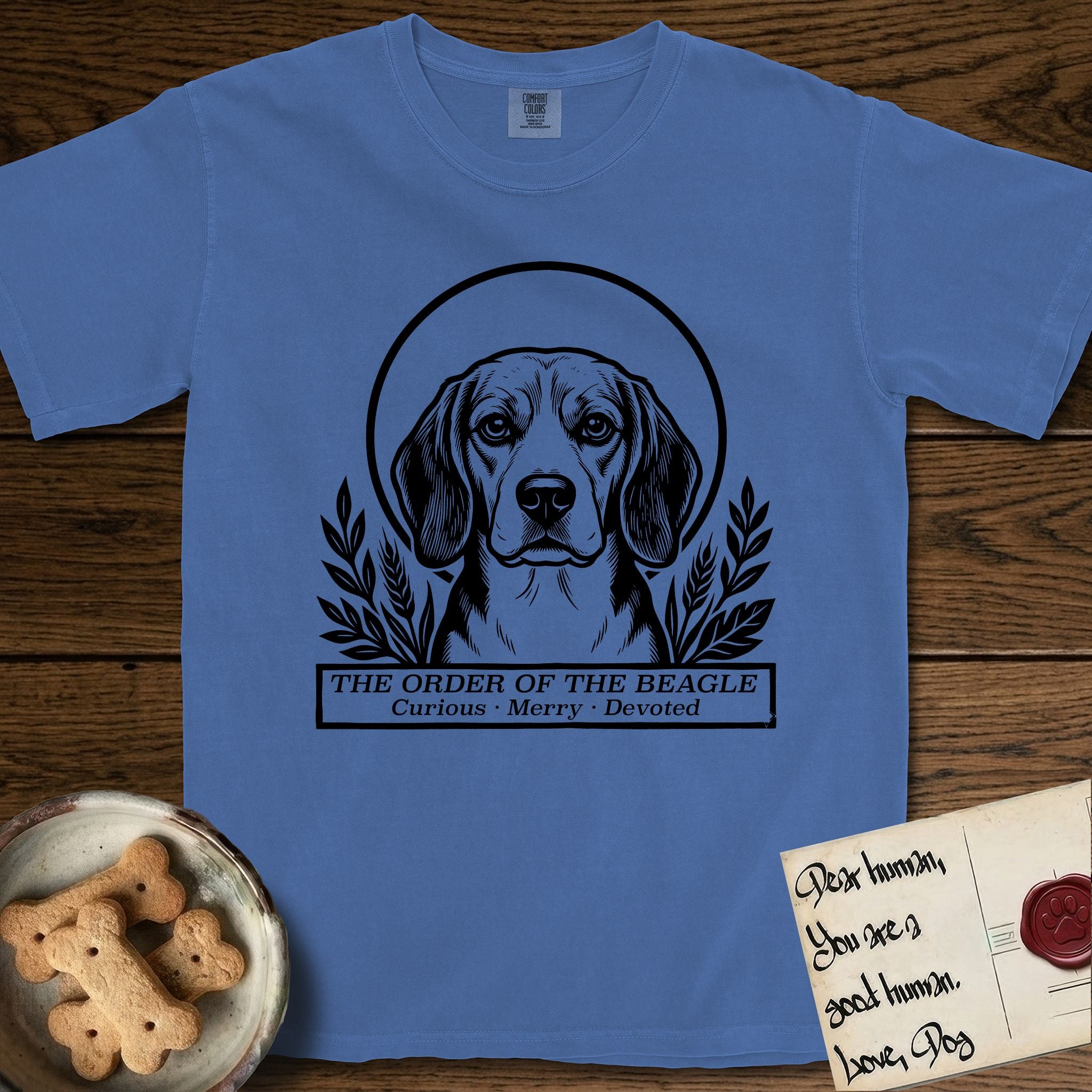 Holy Orders Beagle T-Shirt flat lay in Mystic Blue, featuring a bold black-and-white linocut saint-medallion portrait of a Beagle.