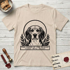 Holy Orders Beagle T-Shirt flat lay in Sand, featuring a bold black-and-white linocut saint-medallion portrait of a Beagle.