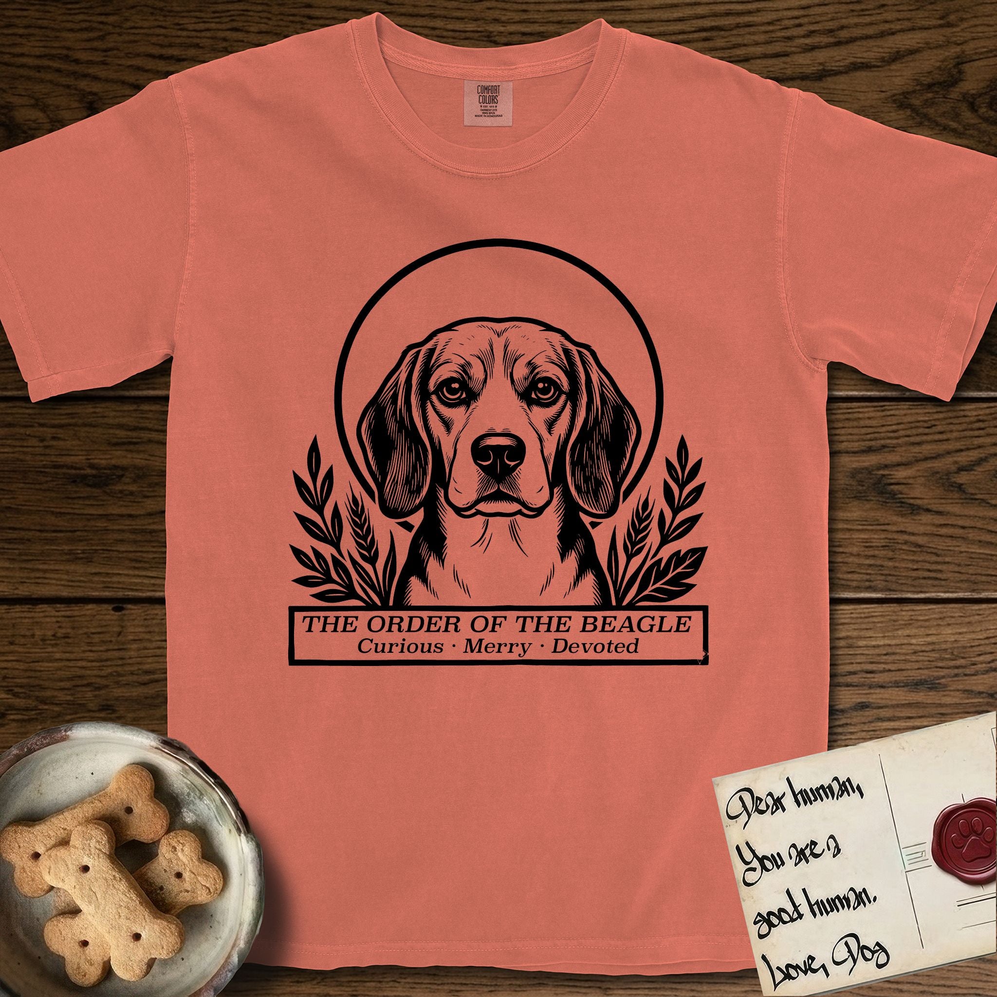 Holy Orders Beagle T-Shirt flat lay in Terracotta, featuring a bold black-and-white linocut saint-medallion portrait of a Beagle.